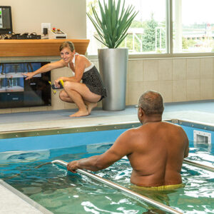 A woman helping a man in a therapy pool.