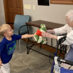 a young boy showing a stuffed animal to an elderly woman