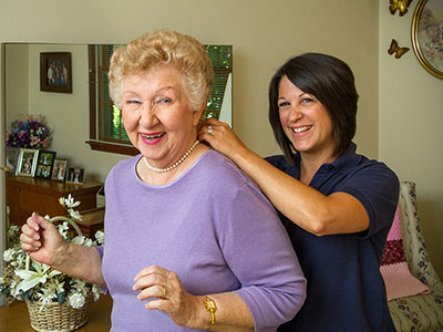 an assistant helping an elderly woman get a necklace on