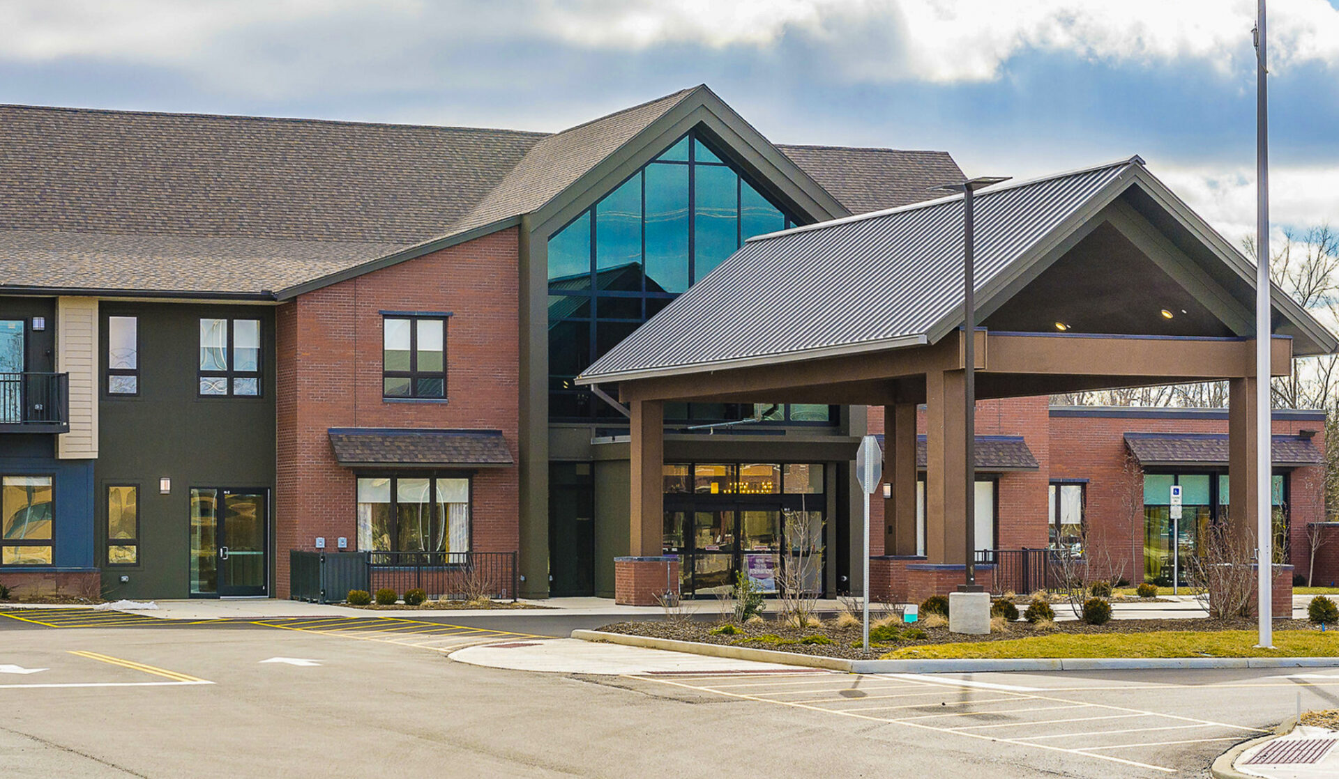 ThePatterson Beaverceek Exterior_web Modern brick and glass community facility exterior with covered entrance, large windows, and landscaped grounds under blue sky
